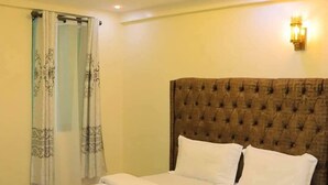 A neatly made bed with a tufted headboard, a wall-mounted light fixture, and a patterned curtain. - Lux Suites Taris Apartments Rongo (Rongo)