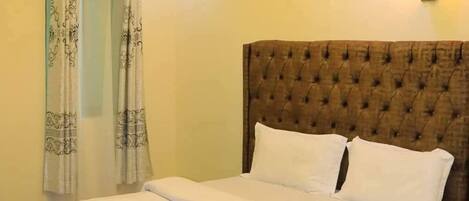 A neatly made bed with a tufted headboard, a wall-mounted light fixture, and a patterned curtain.