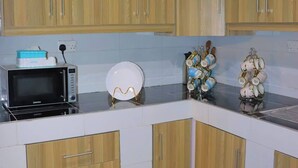 A kitchen with wooden cabinets, a microwave, a kettle, and a decorative vase. - Lux Suites Taris Apartments Rongo (Rongo)