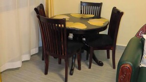 A dining area with a round table, four chairs, and a wall-mounted light fixture. - Lux Suites Taris Apartments Rongo (Rongo)