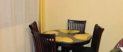 A dining area with a round table, four chairs, and a wall-mounted light fixture.