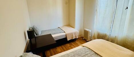 A small, clean room with two beds, a desk, and a radiator.