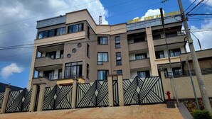 Un immeuble à plusieurs étages, doté d’une entrée sécurisée par un portail, de balcons et surplombant un ciel dégagé.