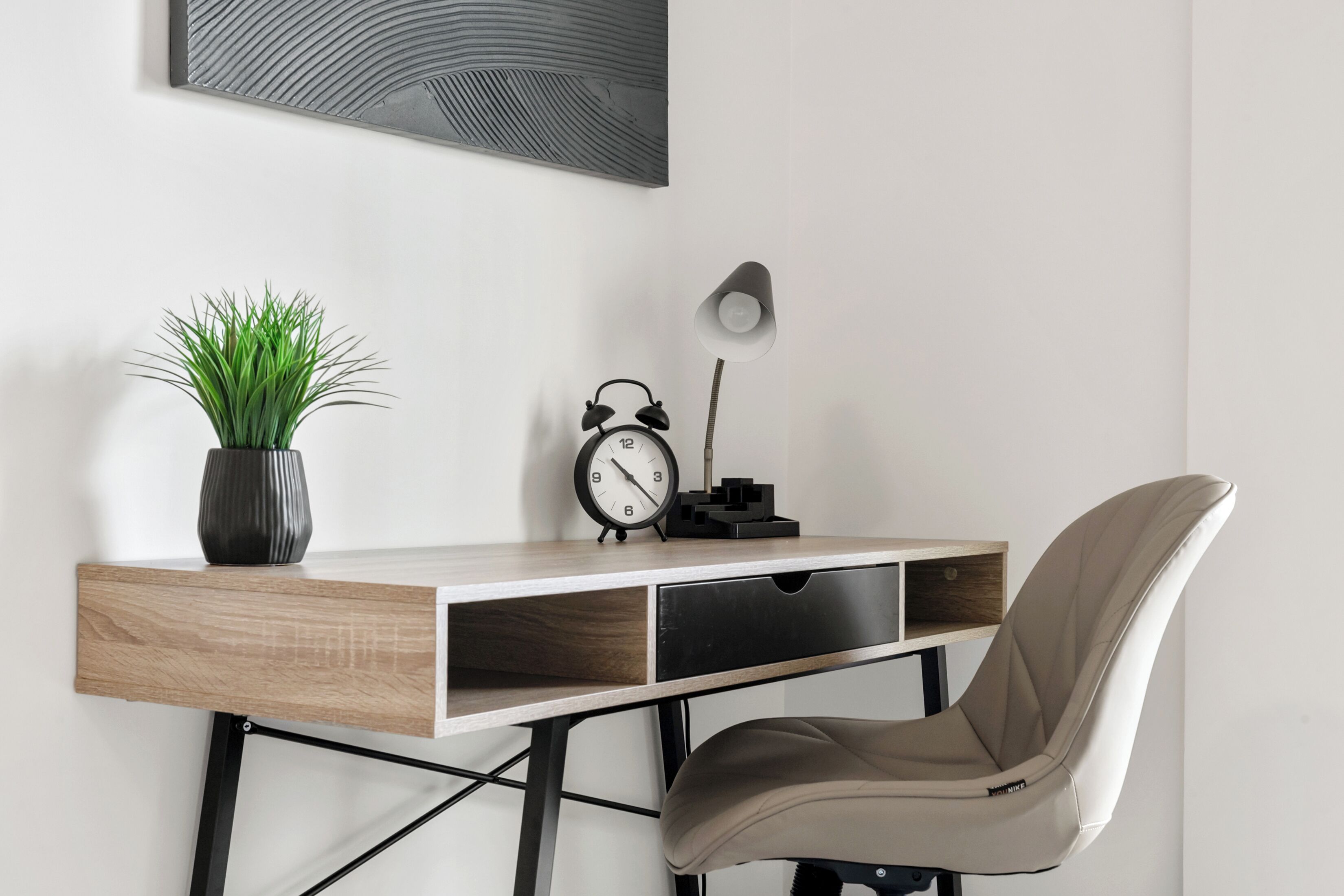 A modern desk with a plant, a clock, and a lamp.