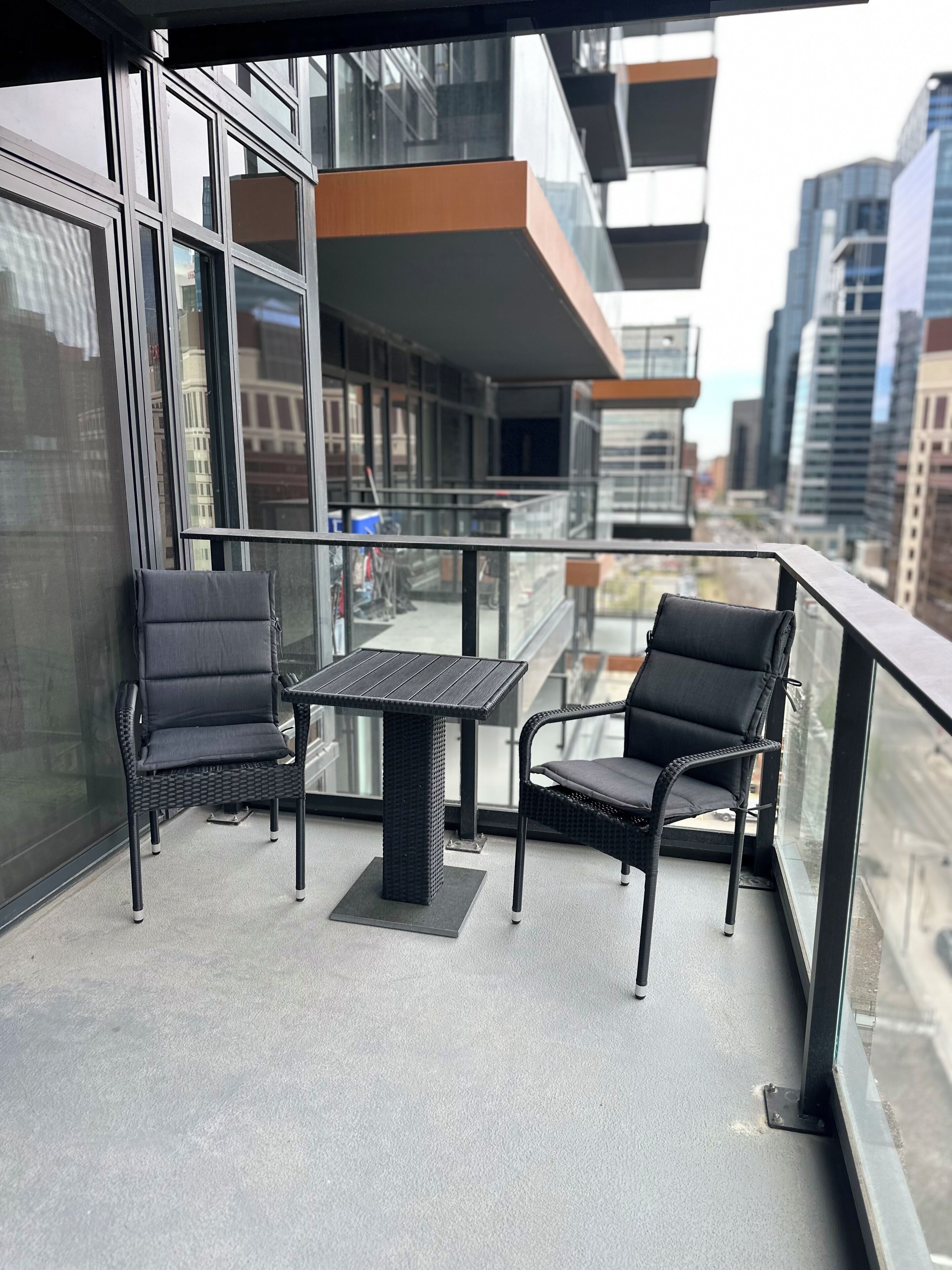 A balcony with two chairs and a table, overlooking a cityscape with modern buildings.