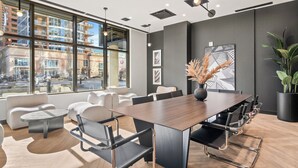 A modern conference room with a large table, comfortable seating, and large windows offering a city view. - Western Dreams w River Views, 2BR, AC (25+) (Calgary)