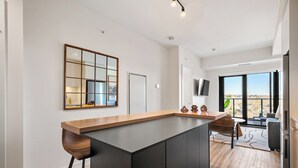 A modern kitchen with a large island, a dining area with a table and chairs, and a large window offering a view. - Western Dreams w River Views, 2BR, AC (25+) (Calgary)