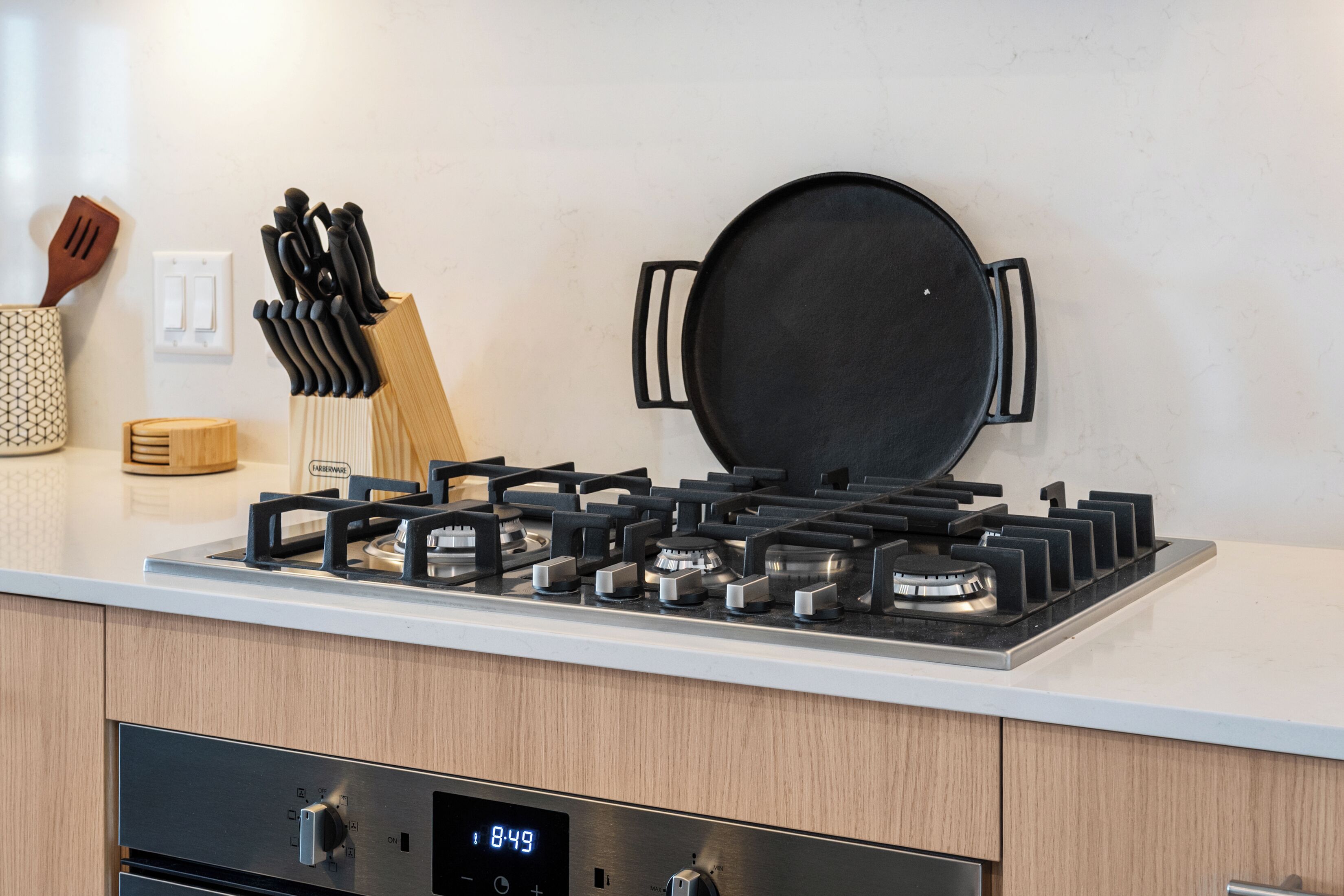A modern kitchen with a gas stove, a digital clock, and a knife block.