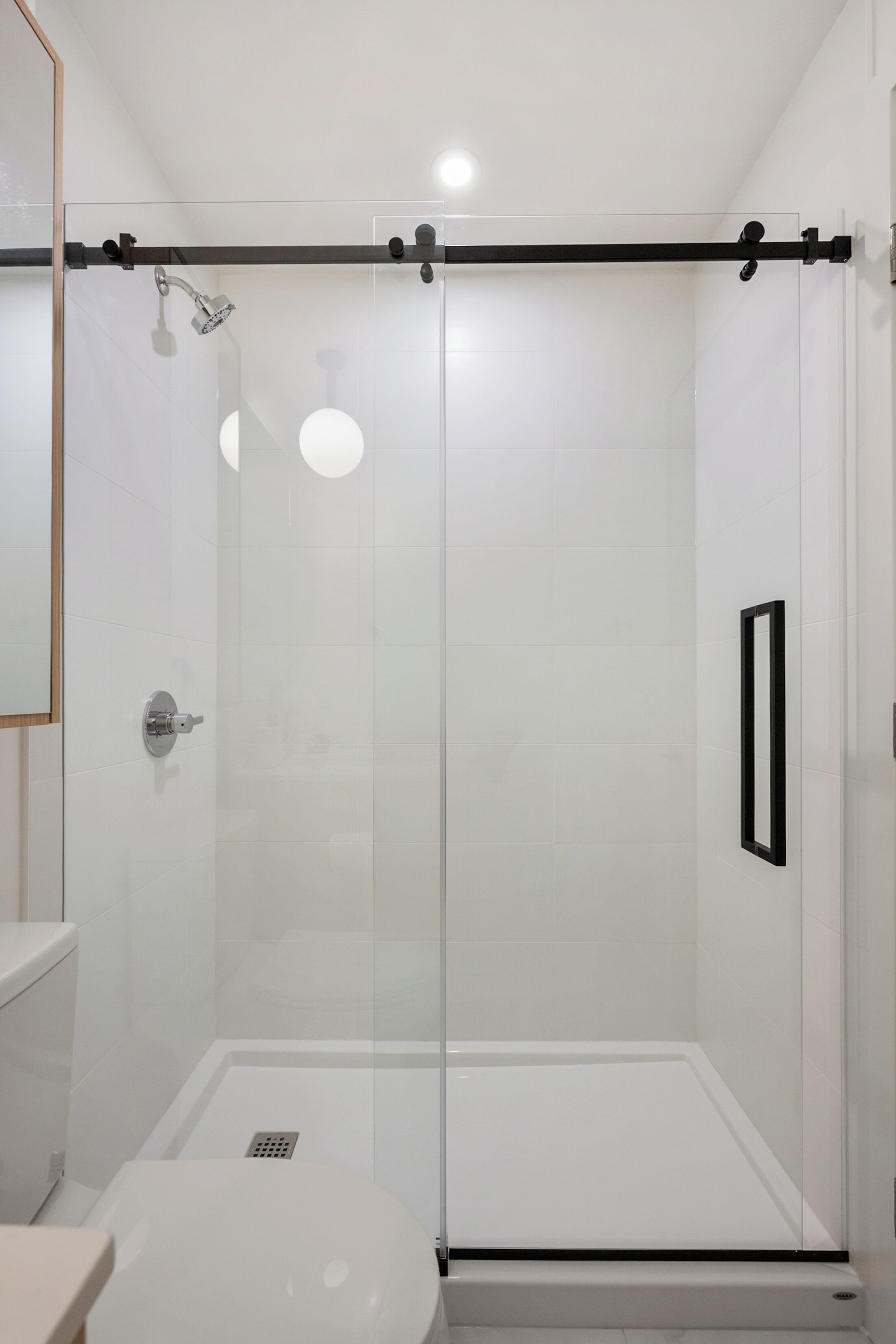 Une salle de bain moderne avec une douche à parois de verre, des toilettes blanches et un miroir.