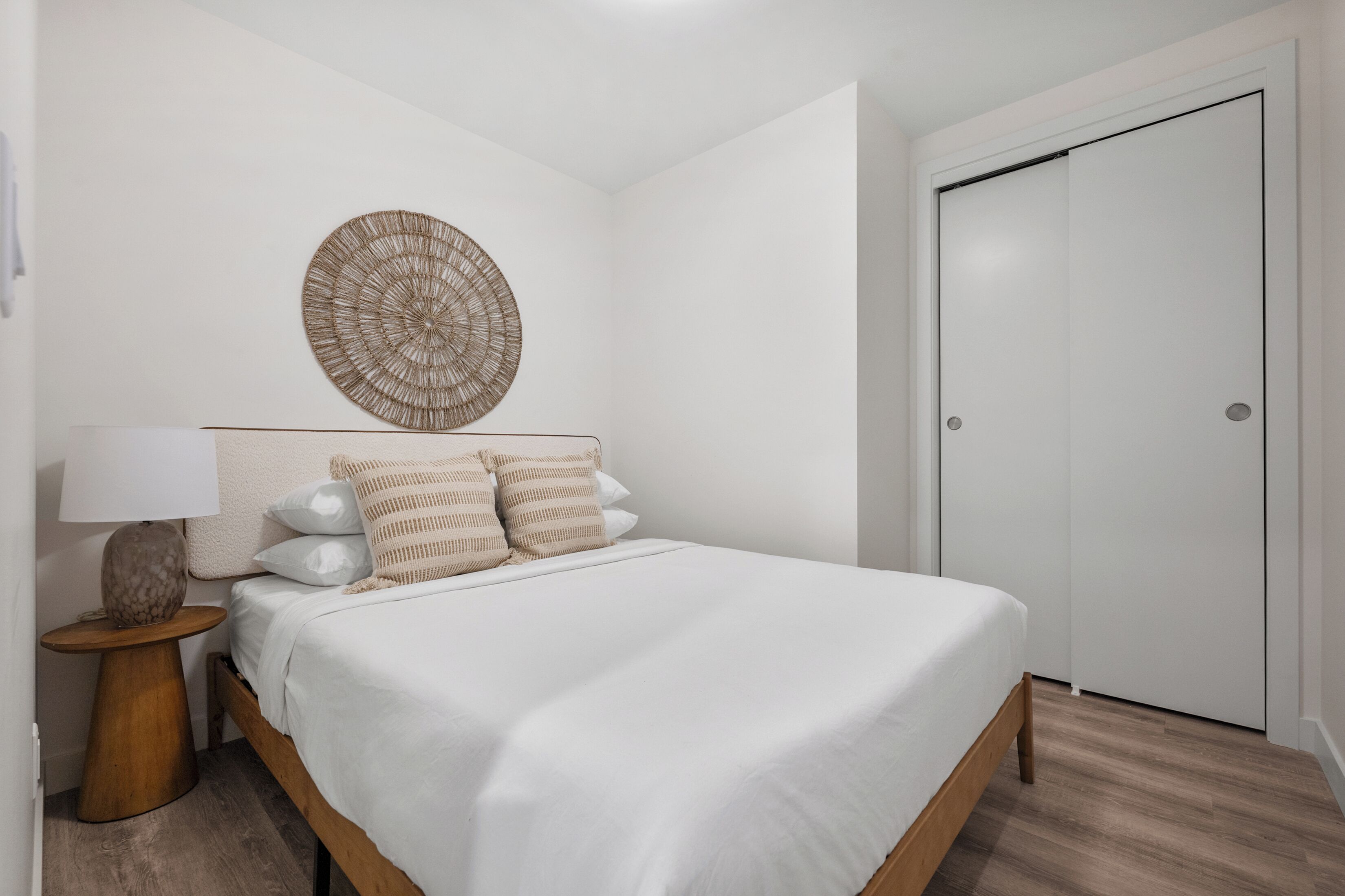 A bedroom with a bed, a round wall decoration, a nightstand, and a white wardrobe.