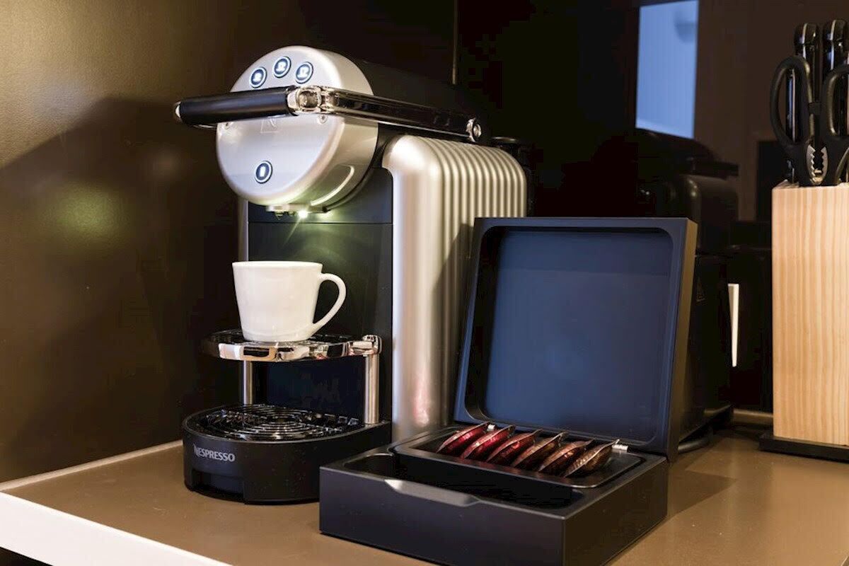 A Nespresso coffee machine with a cup holder and a box of coffee capsules.