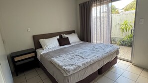 A bedroom with a bed, a nightstand, a ceiling light, and a sliding glass door leading to a balcony. - Sea Spray Suites - Paihia Beachfront Complex - Unit 5 (Paihia)