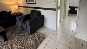 A modern living room with a sofa, a rug, and a lamp. There is a hallway leading to a bathroom with a sink and a window. - Sea Spray Suites - Paihia Beachfront Complex - Unit 5 (Paihia)