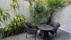A patio area with a round table and four chairs, surrounded by various plants and a wooden fence. - Sea Spray Suites - Paihia Beachfront Complex - Unit 5 (Paihia)