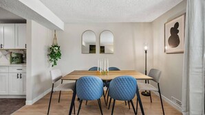 Un coin repas avec une table en bois, quatre chaises bleues et un lustre moderne.