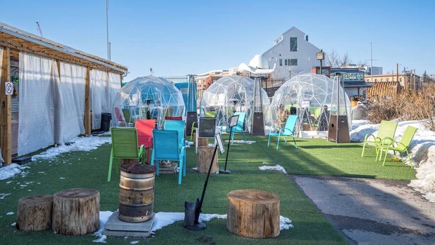 Une cour avec une pelouse artificielle verte, des dômes transparents en plastique et des chaises colorées.