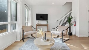 A modern living room with two armchairs, a coffee table, a TV, and a staircase. - The Elevated Escape 5B w/ Rooftop, Parking x4, AC (Calgary)