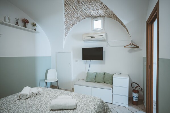 A bedroom with a bed, a TV, a heater, a fire extinguisher, and a window.