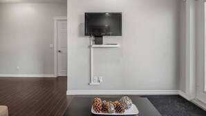 Una sala de estar moderna con un televisor de pantalla plana montado en la pared, un estante blanco debajo y una mesita con objetos decorativos.