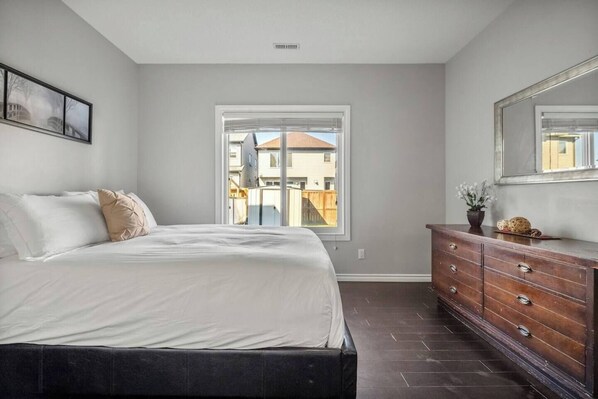 A bedroom with a bed, dresser, and a window with a view of buildings.
