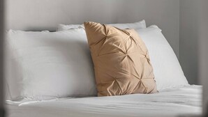 Una cama con ropa blanca y una almohada beige.