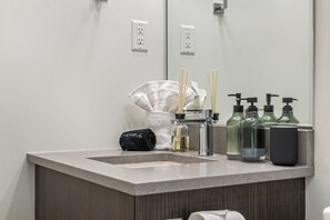A bathroom with a sink, mirror, and toiletries. - Industrial 1BR w Office, Views, AC, XL Patio (Calgary)