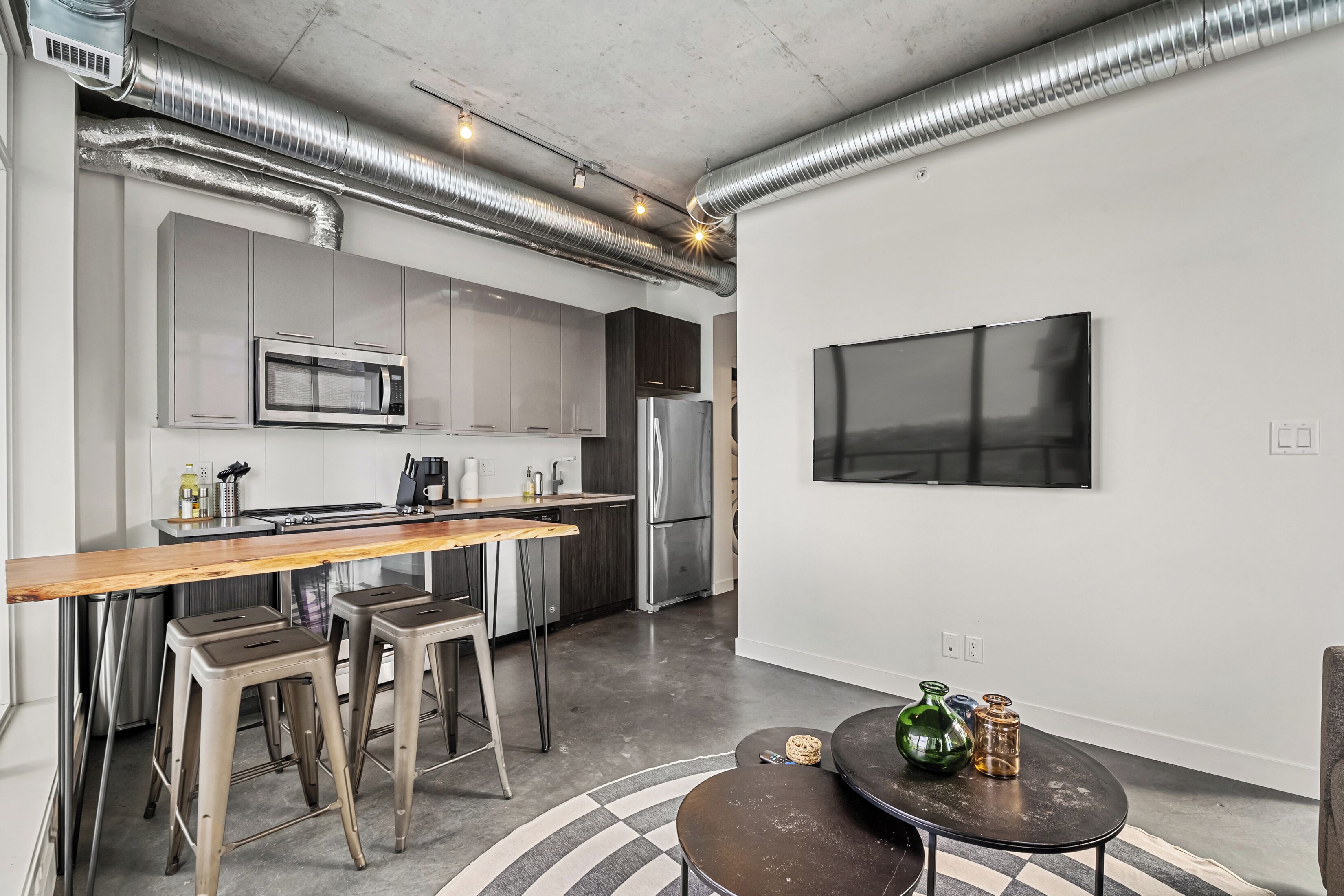 A modern kitchen with stainless steel appliances, a wooden bar counter, and bar stools.