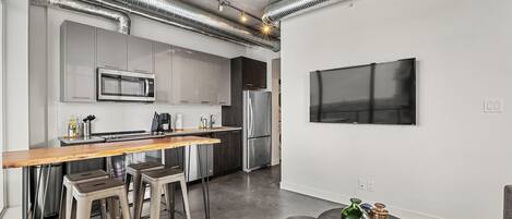 A modern kitchen with stainless steel appliances, a wooden bar counter, and bar stools.