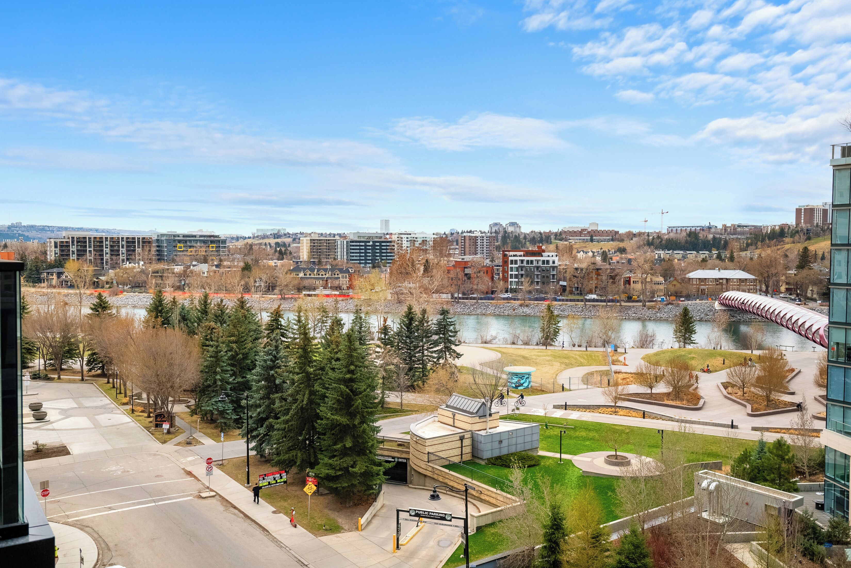 A modern building with a glass facade, a landscaped courtyard, and a view of a river and cityscape.