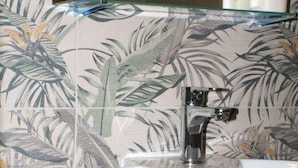 Ein Badezimmer mit einem weißen Waschbecken, einem Spiegel und blumigem Wandpapier.