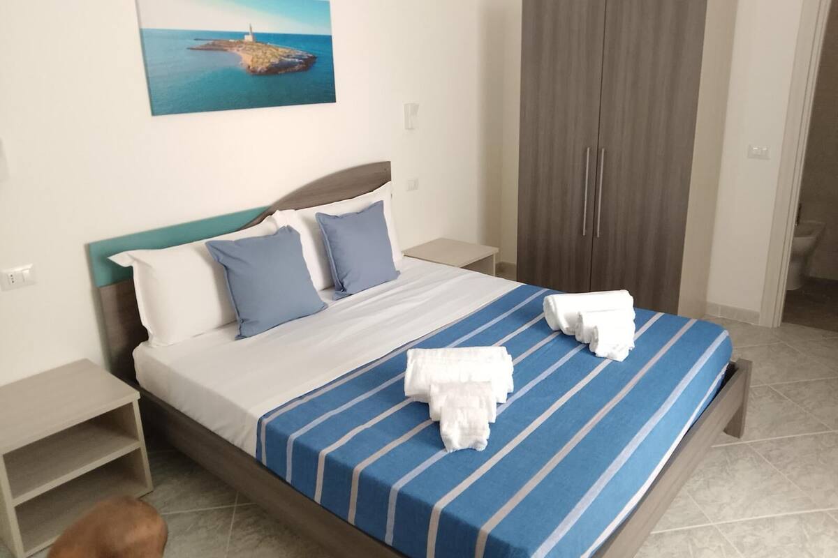 A hotel room with a bed, a wardrobe, a nightstand, and a painting on the wall.