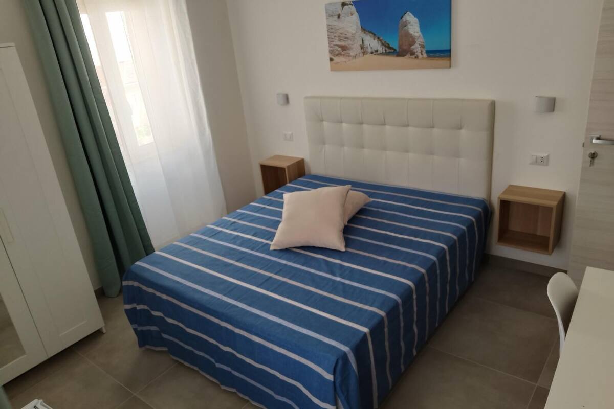 A bedroom with a bed, a headboard, a nightstand, a painting, and a window with curtains.