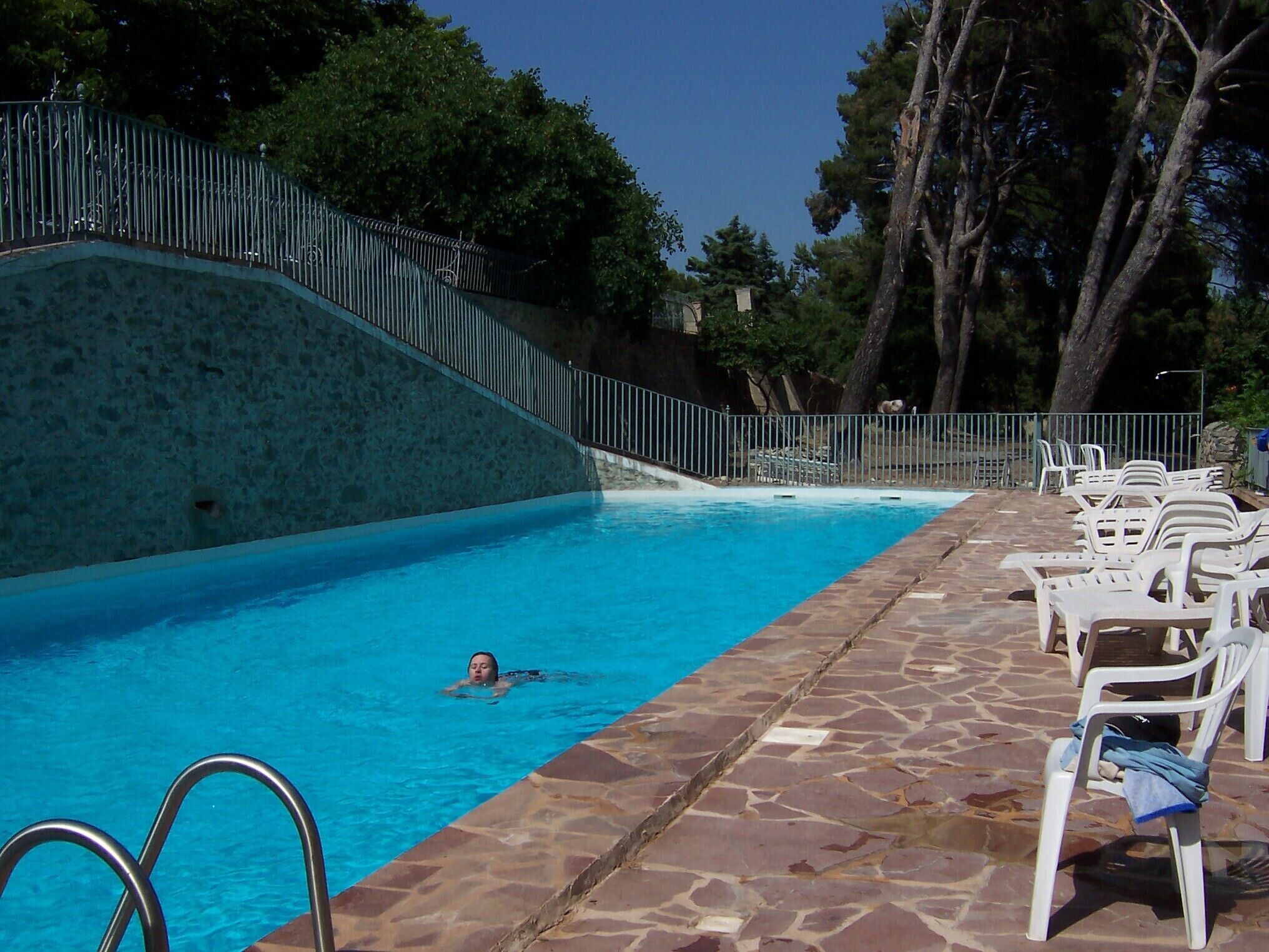 Ein Schwimmbecken mit einer Steindeck und weißen Liegestühlen.