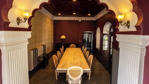 Een eetkamer met een lange houten tafel, witte stoelen en een kroonluchter.