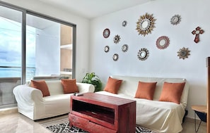 A modern living room with a white sofa set, a wooden coffee table, and decorative wall art. - by Calamari Homes - Altamar Building (Cartagena)