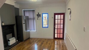 Un pasillo con suelo de madera, una puerta con cortinas estampadas, un vitral y una lámpara fijada a la pared.