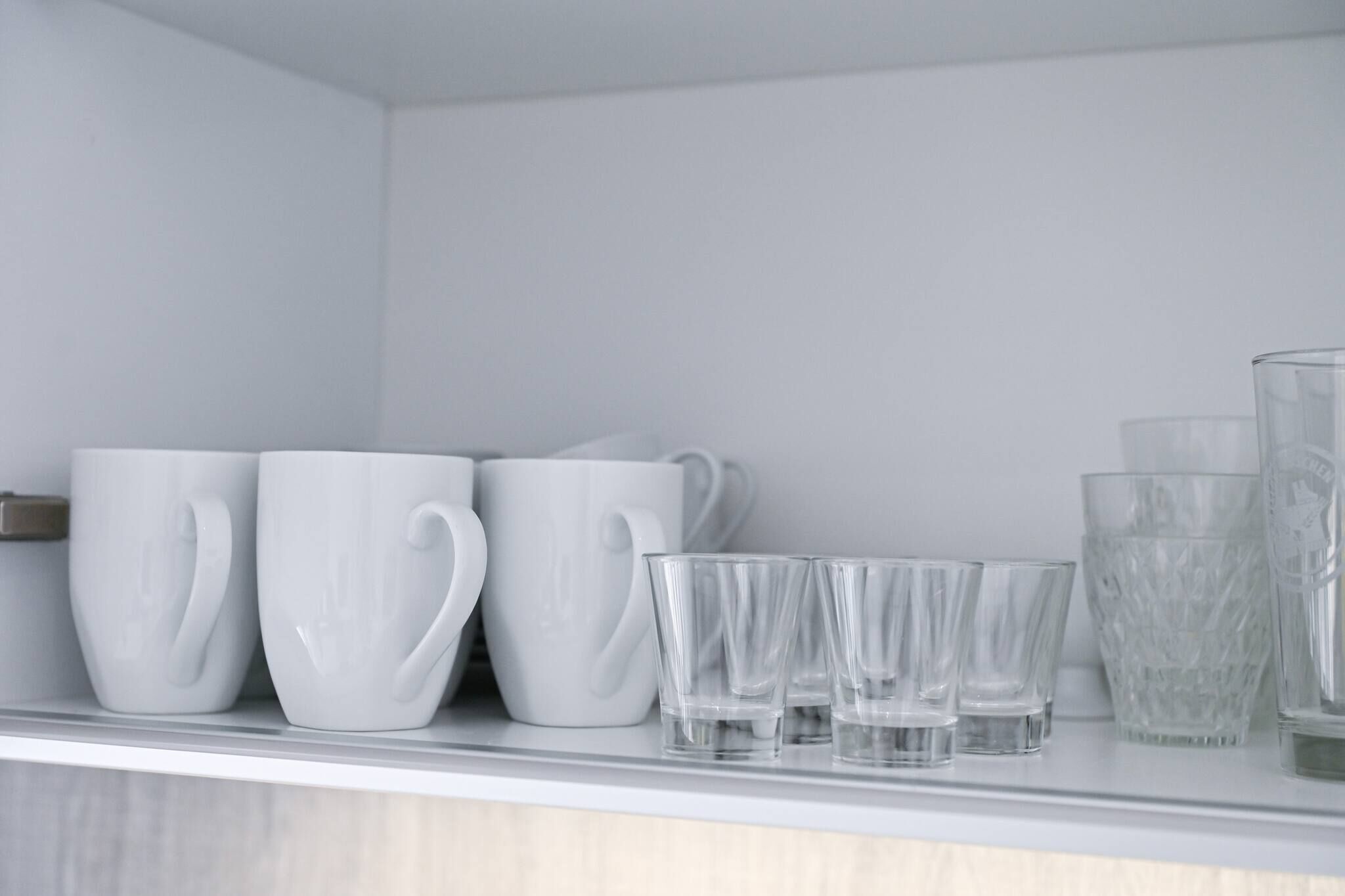 En hylde med hvide keramikkrus og glas.