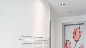 Un couloir avec une armoire blanche, un vase et un mur orné d’une fresque florale.