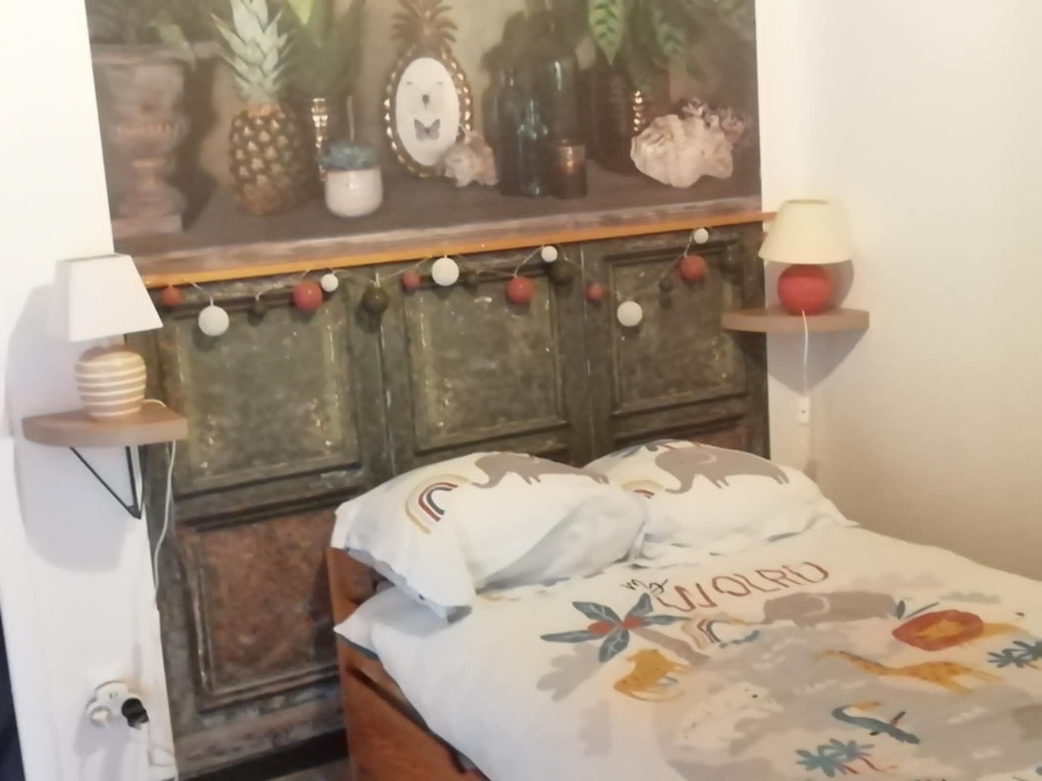 Une chambre à coucher comprenant un lit, une table de chevet, une étagère murale décorative et un mur orné d’un motif peint.