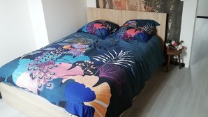 Ein Bett mit farbenfroher Bettdecke und zwei Kissen, ein hölzernes Kopfteil sowie eine Wand mit einem Wandgemälde zum Thema Natur.