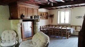Ein Zimmer mit Essbereich, einem gepolsterten Sessel, einem Holzkabinett und einem Fenster.