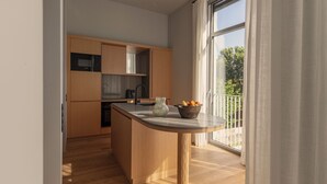 Eine moderne Küche mit Holzschränken, einer zentralen Kochinsel und Blick ins Freie durch große Fenster.