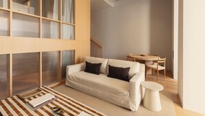 Ein modernes Wohnzimmer mit einer Couch, einem kleinen runden Tisch und einem Essbereich mit einem Holztisch und Stühlen.