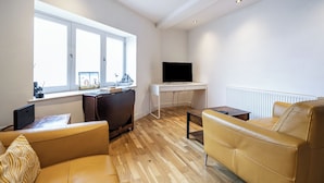 A modern living room with a sofa, a desk, a television, and a window. - Seaside Cottage Escape in Paignton - Sleeps 4 (Paignton)