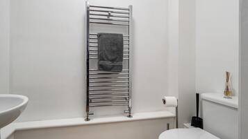 Un baño con un lavamanos blanco, un toallero con una toalla, un inodoro y un rollo de papel higiénico.