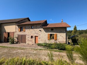 A stone house with a tiled roof, wooden shutters, and a small garden.