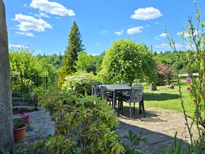 A patio with a table and chairs, surrounded by lush greenery and flowering plants.