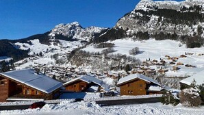 Een bergdorpslandschap bedekt met sneeuw, met houten hutten en een helderblauwe lucht.