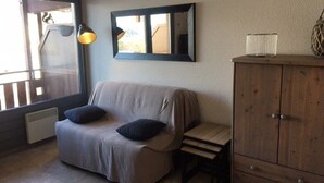 Een gezellige kamer met een grijze bank, twee zwarte kussens, een houten kast en een vloerlamp.