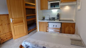 Een compacte slaapkamer met een bed, een houten garderobe, een inbouwkbank en een kitchenette met een magnetron.